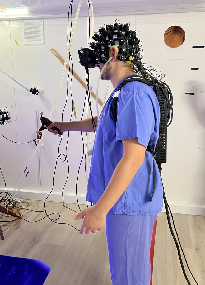 Das Bild zeigt eine Hilfskraft - von Prof. Dominik Bachs Team am University College London mit Messhelm und dem Prototyp der neuen OPMEG-kompatiblen VR-Brille.