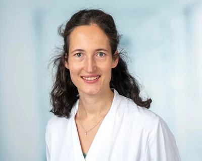 Eine Wissenschaftlerin und ein Wissenschaftler arbeiten hinter einer Glasfassade und mischen Chemikalien mit Großgeräten.