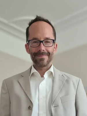 Eine Wissenschaftlerin und ein Wissenschaftler arbeiten hinter einer Glasfassade und mischen Chemikalien mit Großgeräten.