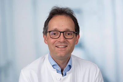 Eine Wissenschaftlerin und ein Wissenschaftler arbeiten hinter einer Glasfassade und mischen Chemikalien mit Großgeräten.
