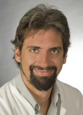 Eine Wissenschaftlerin und ein Wissenschaftler arbeiten hinter einer Glasfassade und mischen Chemikalien mit Großgeräten.