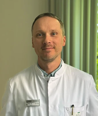 Eine Wissenschaftlerin und ein Wissenschaftler arbeiten hinter einer Glasfassade und mischen Chemikalien mit Großgeräten.