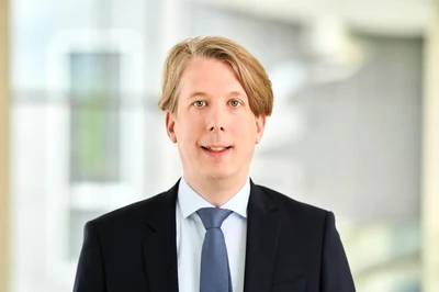 Eine Wissenschaftlerin und ein Wissenschaftler arbeiten hinter einer Glasfassade und mischen Chemikalien mit Großgeräten.