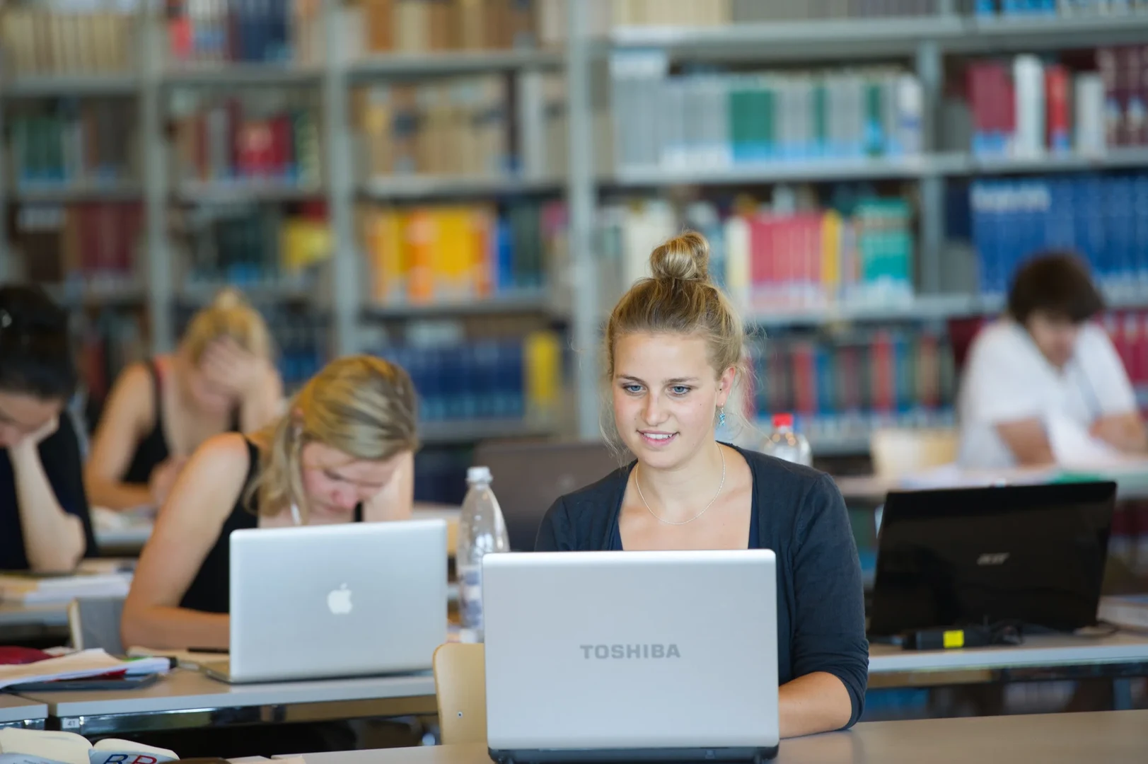 Eine Wissenschaftlerin und ein Wissenschaftler arbeiten hinter einer Glasfassade und mischen Chemikalien mit Großgeräten.