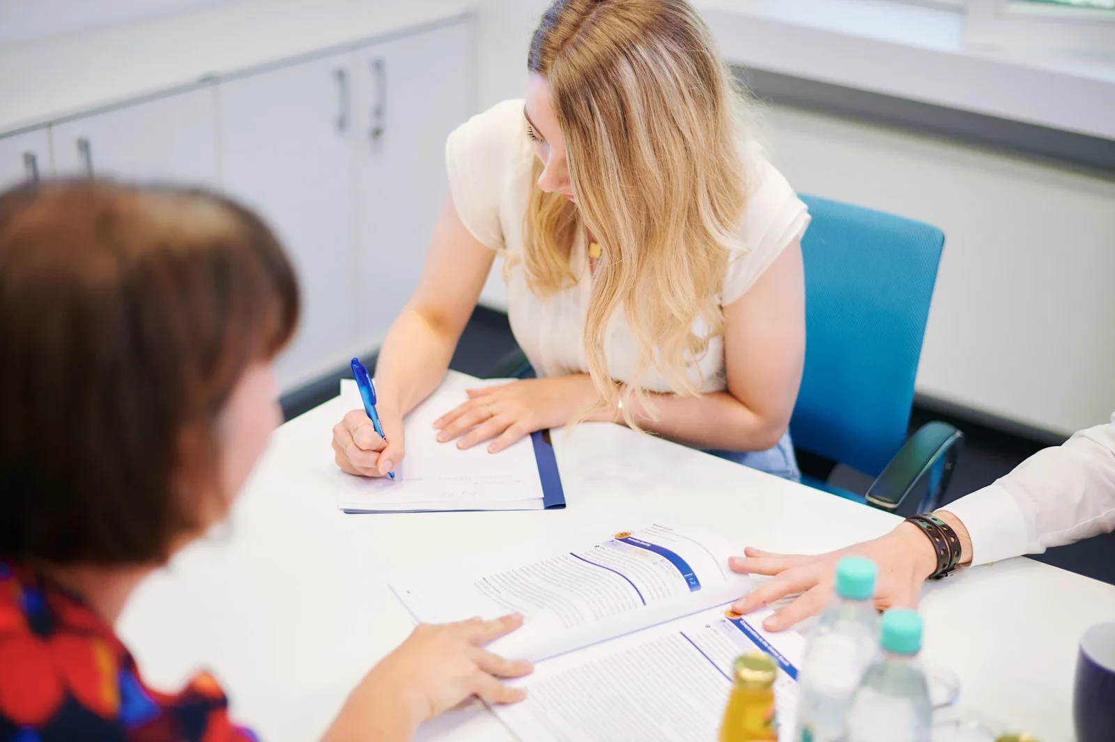 Eine Wissenschaftlerin und ein Wissenschaftler arbeiten hinter einer Glasfassade und mischen Chemikalien mit Großgeräten.