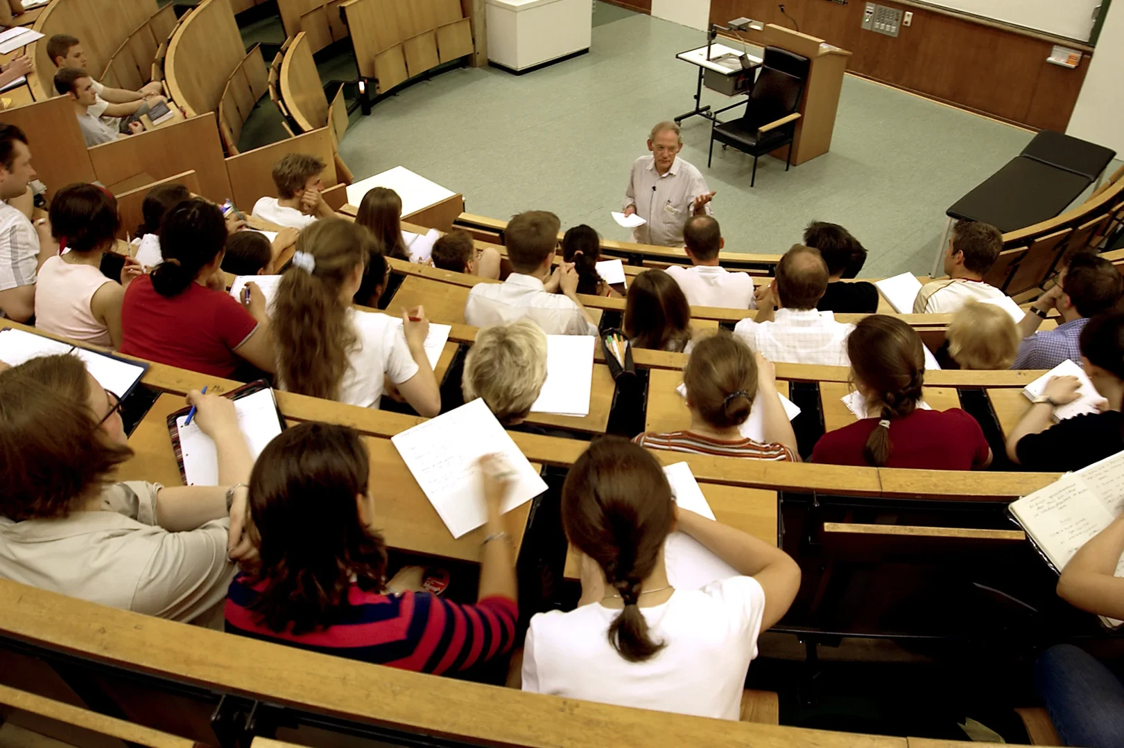 Eine Wissenschaftlerin und ein Wissenschaftler arbeiten hinter einer Glasfassade und mischen Chemikalien mit Großgeräten.