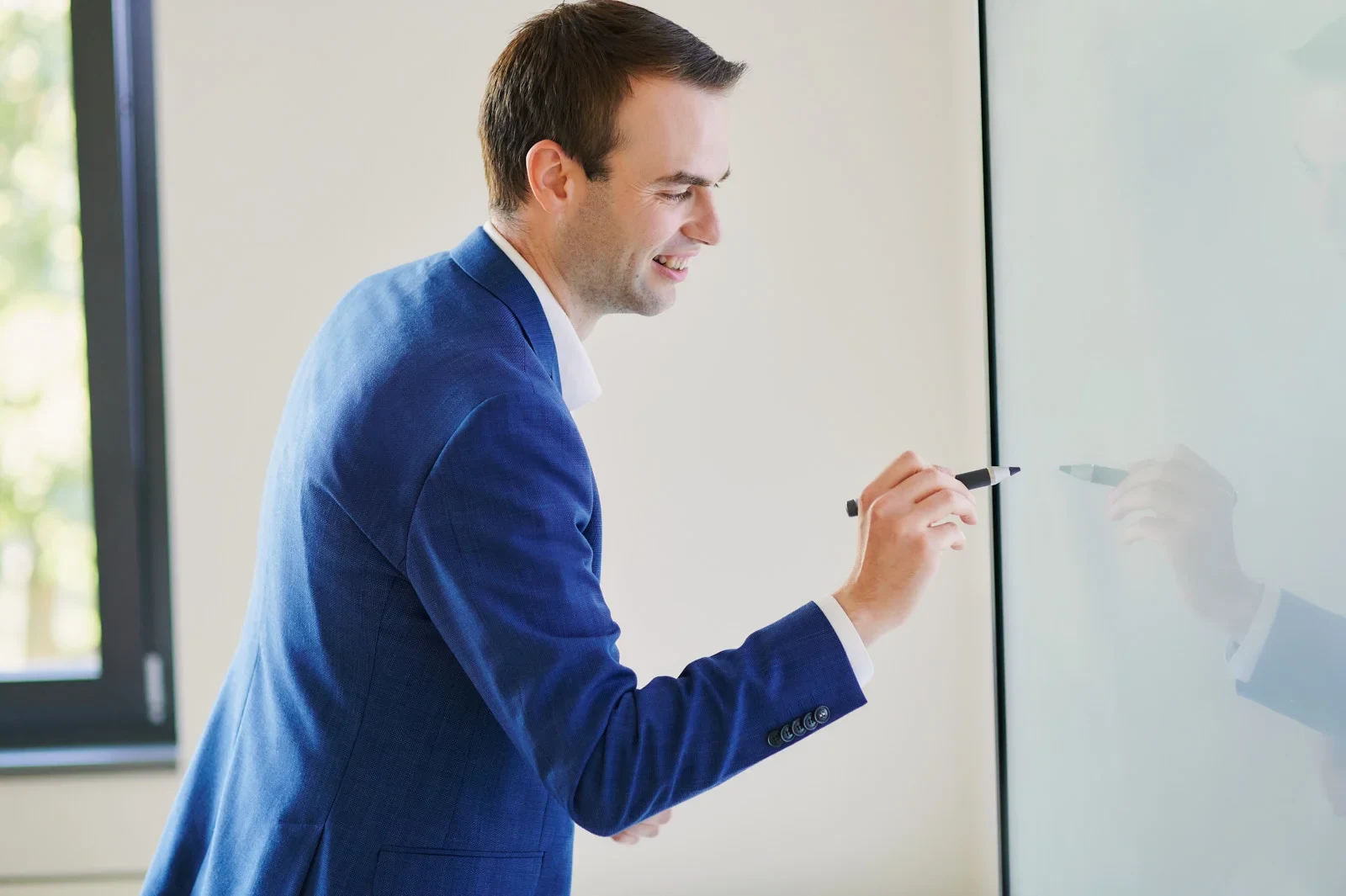 Eine Wissenschaftlerin und ein Wissenschaftler arbeiten hinter einer Glasfassade und mischen Chemikalien mit Großgeräten.