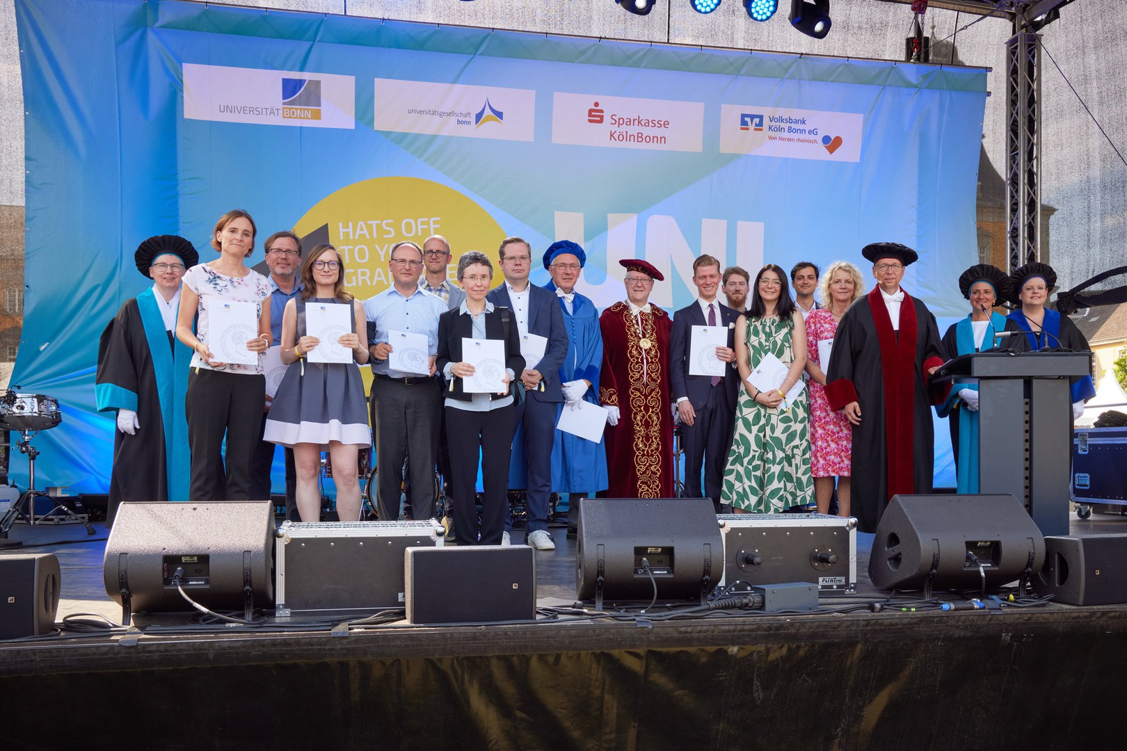 Lehrpreise 2023 - 13 of the 14 award-winning teachers received their certificates in person at the university festival. Also in the picture: Dean and award-winner Prof. Walter Witke (light blue gown), Rector Prof. Michael Hoch (red gown), Vice Rector Prof. Irmgard Förster (left, black-blue gown), Vice Rector Prof. Annette Scheersoi (right, black-light blue gown) , Vice Rector Prof. Birgit Ulrike Münch (right, black-dark blue gown) and Vice Rector Prof. Klaus Sandmann (black-red gown).