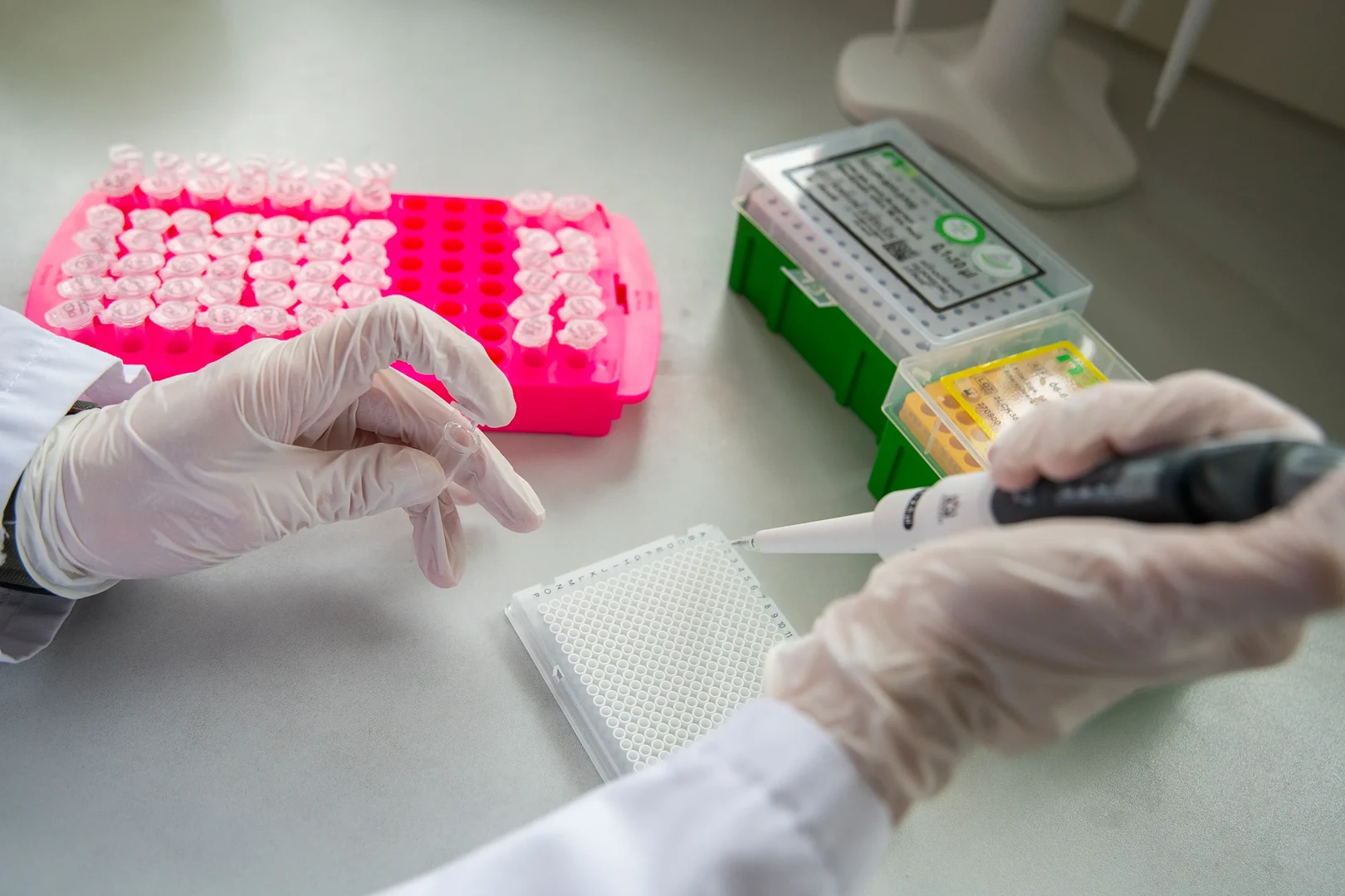 Eine Wissenschaftlerin und ein Wissenschaftler arbeiten hinter einer Glasfassade und mischen Chemikalien mit Großgeräten.