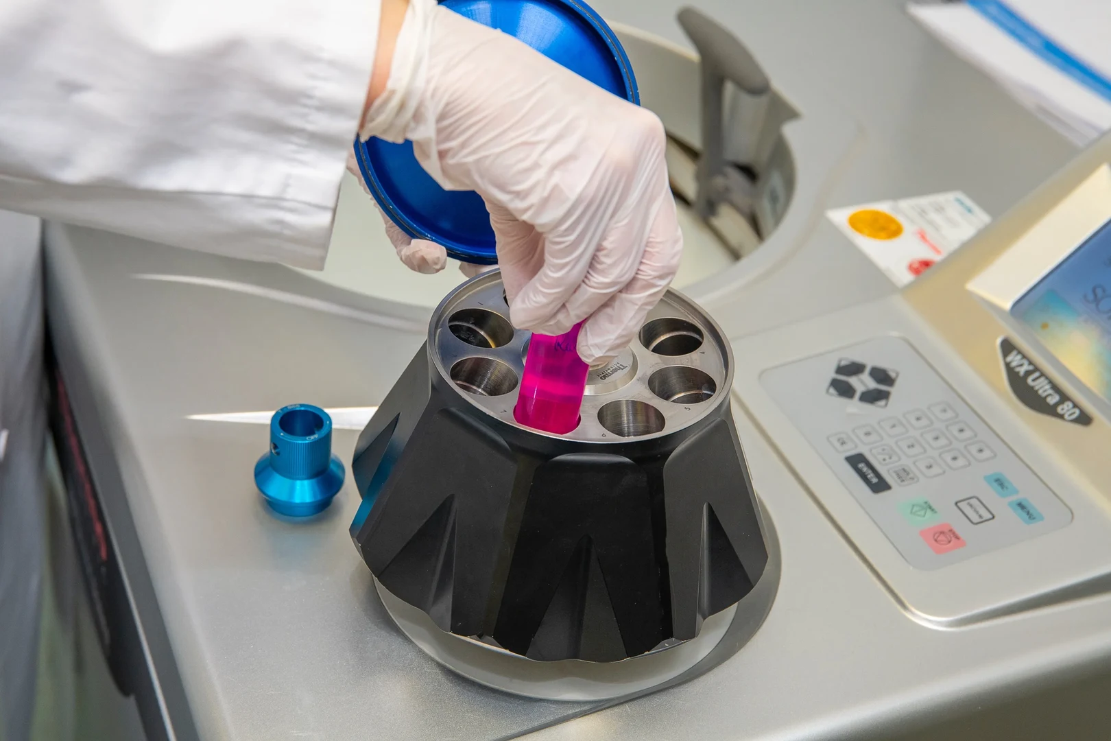 Eine Wissenschaftlerin und ein Wissenschaftler arbeiten hinter einer Glasfassade und mischen Chemikalien mit Großgeräten.